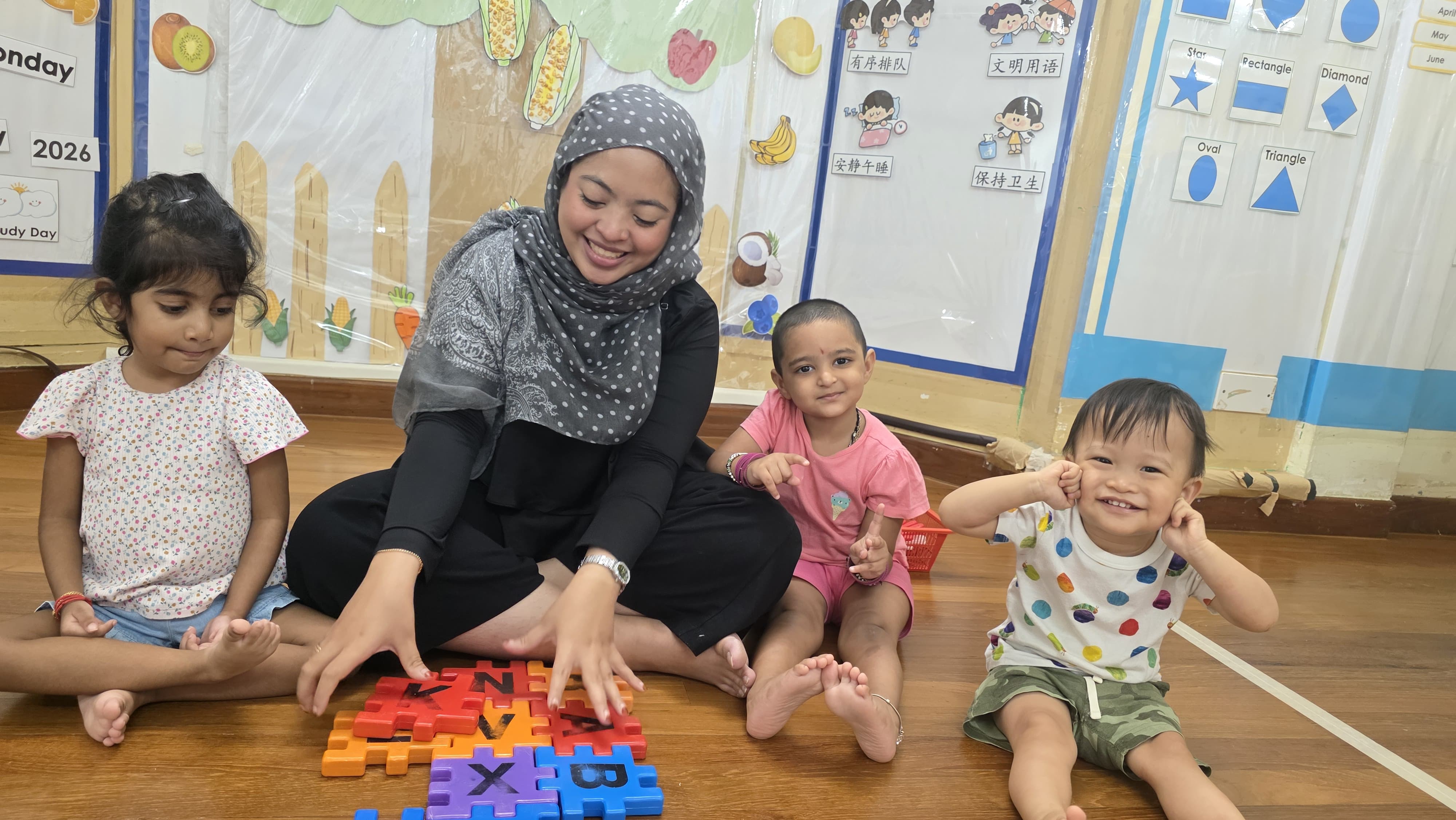 Teacher and children playing with colourful letter puzzles on the classroom floor at Genius Gems Childcare Centre